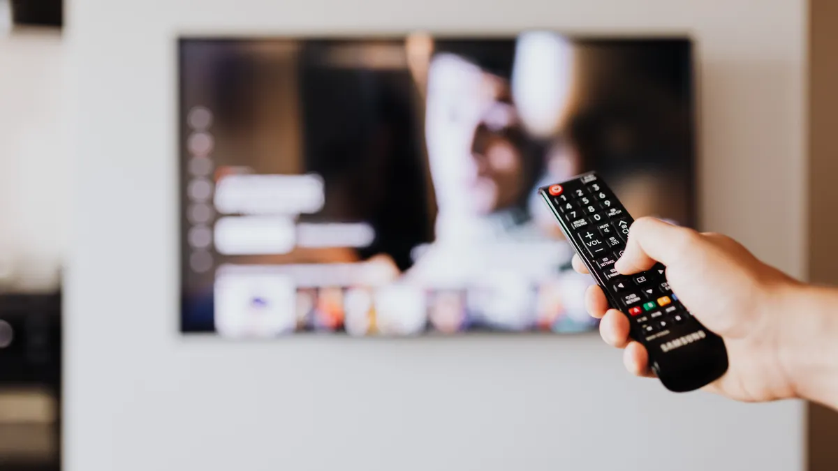 Person med fjernkontroll foran TV som viser hva IPTV er i praksis
